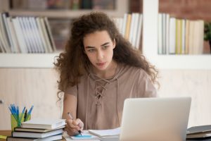 Teen college graduate student studying looking at laptop making notes